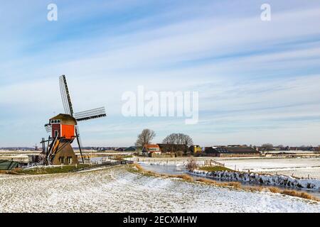 Scène d'hiver hollandaise emblématique, patinage sur glace dans un paysage de polder avec le Rode Molen, un moulin de poste historique à Oud Ade, Hollande du Sud, pays-Bas. Banque D'Images