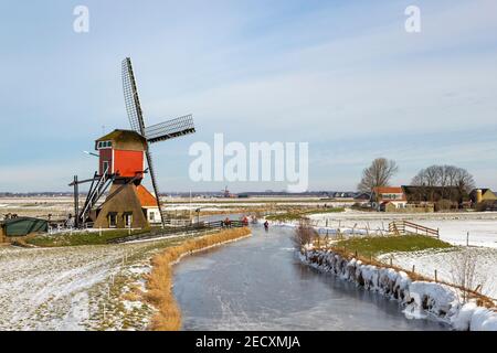 Scène d'hiver hollandaise emblématique, patinage sur glace dans un paysage de polder avec le Rode Molen, un moulin de poste historique à Oud Ade, Hollande du Sud, pays-Bas. Banque D'Images