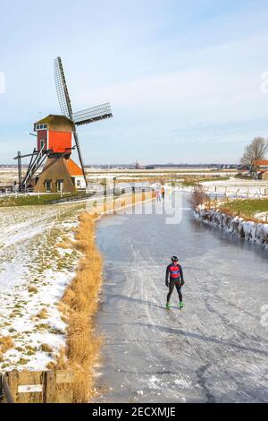 Scène d'hiver hollandaise emblématique, patinage sur glace dans un paysage de polder avec le Rode Molen, un moulin de poste historique à Oud Ade, Hollande du Sud, pays-Bas. Banque D'Images