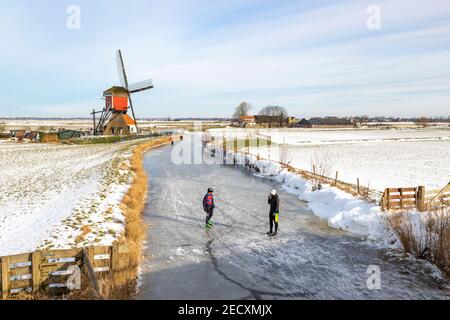 Scène d'hiver hollandaise emblématique, patinage sur glace dans un paysage de polder avec le Rode Molen, un moulin de poste historique à Oud Ade, Hollande du Sud, pays-Bas. Banque D'Images