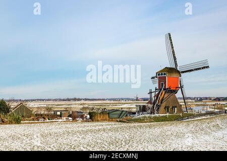 Scène d'hiver hollandaise emblématique, patinage sur glace dans un paysage de polder avec le Red Mill, un moulin de poste historique à Oud Ade, Hollande du Sud, pays-Bas. Banque D'Images