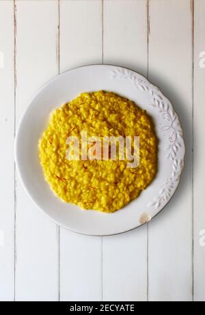 Risotto alla milanais habillé de fils de safran et d'une croûte de fromage Parmigiano Reggiano sur une table en bois blanc. Cuisine italienne. Banque D'Images