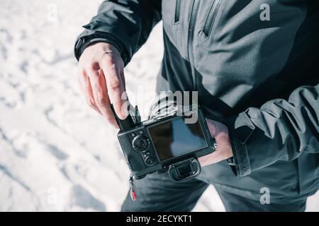 Mains d'un photographe insérant la batterie dans son appareil photo professionnel dans la neige. Banque D'Images