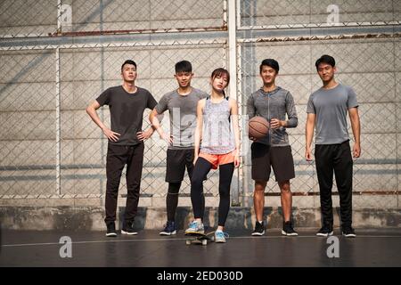 hipster jeune femme asiatique posant à l'extérieur avec un skateboard et quatre amis masculins Banque D'Images