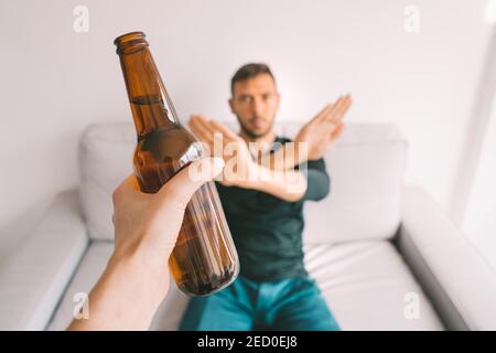 Pas d'alcool. Arrêter l'alcoolisme. Un jeune homme refuse de boire de la bière, montrant un signe de rejet sur une bouteille de bière Banque D'Images