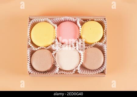 Emballage de macarons colorés dans une boîte en carton sur fond beige vue de dessus Banque D'Images