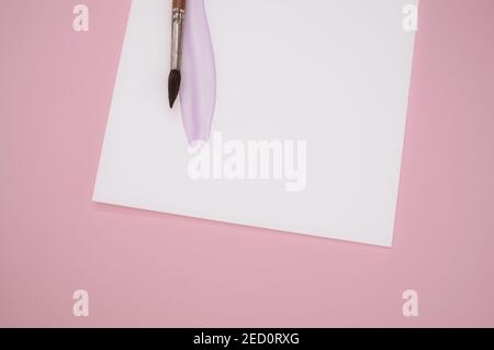 Gros plan d'aquarelle violette sur une feuille de papier avec une brosse sur fond rose Banque D'Images