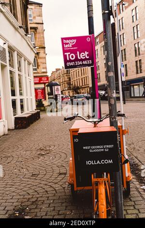 Orange tricycle annonçant iolla.com et Happy laisse faire une publicité sur un lampost, en direction de Band Supplies and substance BMX sur Old Dumbarton Road à fin Banque D'Images