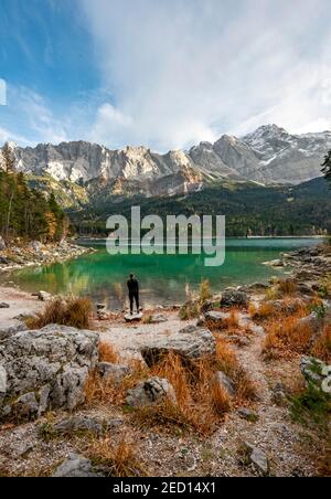 Jeune femme debout sur le rivage, lac d'Eibsee avec Zugspitzmassif et Zugspitze, montagnes de Wetterstein, près de Grainau, haute-Bavière, Bavière, Allemagne Banque D'Images