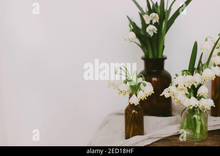 Fleurs blanches printanières dans des bouteilles en verre rétro sur du linge rustique et du bois dans la chambre. La vie rurale encore. Bonjour printemps. Jardinage et botanique. FIR Banque D'Images