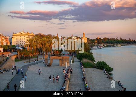 Promenade au bord de l'eau Muelle de la sal au fleuve Rio Guadalquivir avec Monumento a la Tolerancia et Torre del Oro, coucher de soleil, Séville, Andalousie Banque D'Images