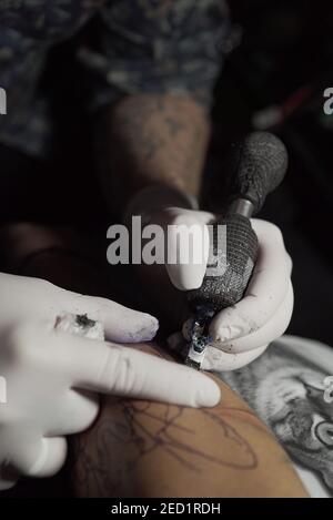 Par-dessus le tatoueur mâle méconnaissable en utilisant la machine et la fabrication tatouage sur le bras de la récolte client en salon Banque D'Images