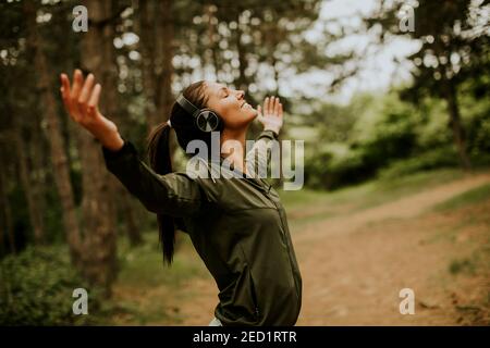 Jolie jeune femme avec des écouteurs qui la préécoute dans les bras de la forêt parce qu'elle aime l'entraînement à l'extérieur Banque D'Images