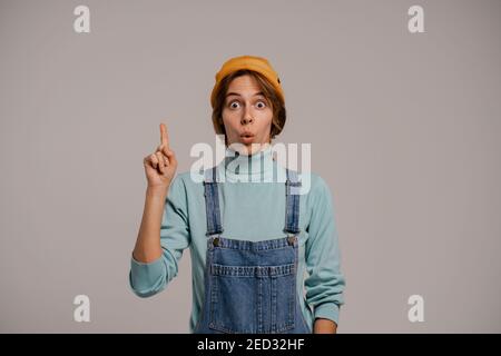 Photo d'une jolie culotte taille basse, semble avoir une idée. Blanc femme porte une combinaison en denim et chapeau isolé de couleur grise fond Banque D'Images