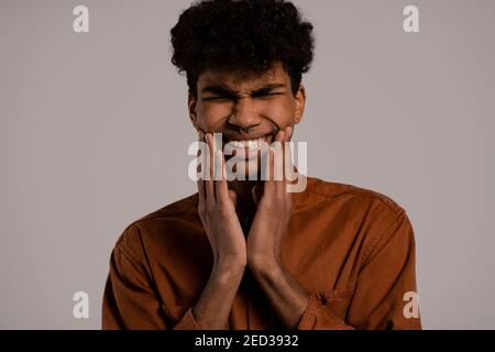 La photo de l'homme noir semble avoir des douleurs dans les dents. Homme porte une chemise, arrière-plan gris isolé Banque D'Images