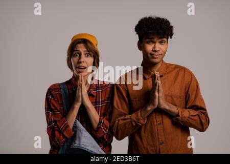 Photo de couple mignon agriculteurs s'inquiètent et prient pour quelque chose. Blanc femme porte une combinaison en denim, noir homme chemise isolé couleur marron fond Banque D'Images