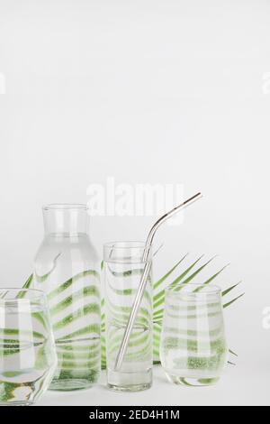 feuille de palmier déformée à travers l'eau dans des verres et une bouteille avec tube réutilisable sur fond blanc.décor de maison, écologique, concept d'eau pure.espace de copie Banque D'Images