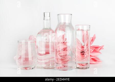 fleurs roses déformées par l'eau dans les verres et la bouteille sur fond blanc. Décoration maison, écologique, détente, concept de jardinage. Banque D'Images