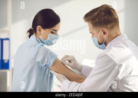 Homme travailleur médical dans le masque mettant le plâtre à la femme patient bras après la vaccination contre le coronavirus Banque D'Images