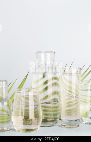 feuille de palmier déformée dans l'eau dans les verres et les bouteilles sur fond bleu. Décoration de maison, écologique, eau pure, concept de jardinage.nature fond Banque D'Images