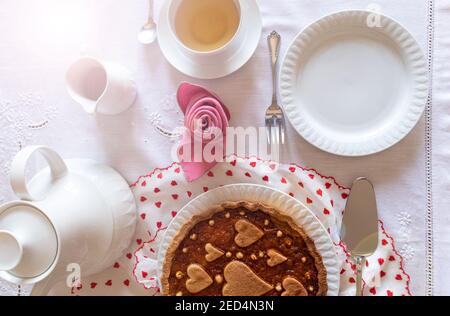 Une table pour un petit déjeuner spécial. Une tarte à l'orange sur le tissu de la Saint-Valentin est servie avec une tasse de thé près d'une serviette pliée comme une rose. Banque D'Images