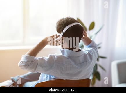 Homme méconnaissable écoutant de la musique dans un casque sans fil à la maison, vue arrière Banque D'Images