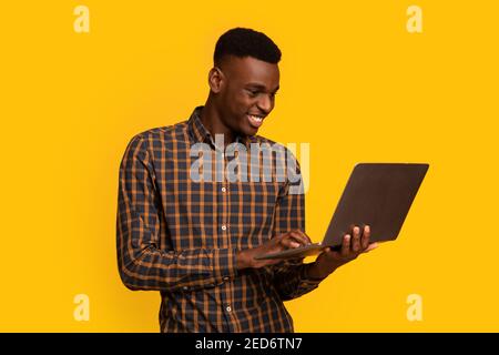 Travail indépendant. Portrait d'un homme africain souriant utilisant un ordinateur portable sur fond jaune Banque D'Images