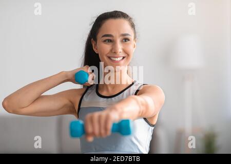 Gros plan de la jeune femme positive faisant l'entraînement de haltères à la maison Banque D'Images
