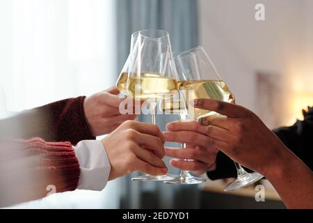 Les mains de jeunes amis interculturels ou de gens d'affaires qui se rabattent flûtes de champagne tout en toaster pour l'anniversaire ou un autre événement Banque D'Images