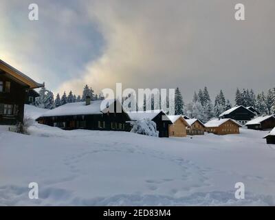 Les cabanes se trouvent sur la piste de ski fraîchement enneigée. village de vacances avec maisons en bois alpin en face d'une forêt de sapins enneigés. Bödele Banque D'Images