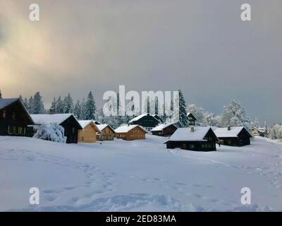 Les cabanes se trouvent sur la piste de ski fraîchement enneigée. village de vacances avec maisons en bois alpin en face d'une forêt de sapins enneigés. Bödele Banque D'Images