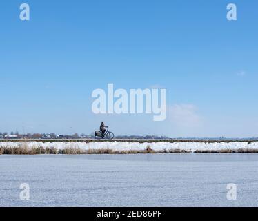 femme en vélo dans le paysage hollandais d'hiver avec canal gelé promenades sur la digue Banque D'Images