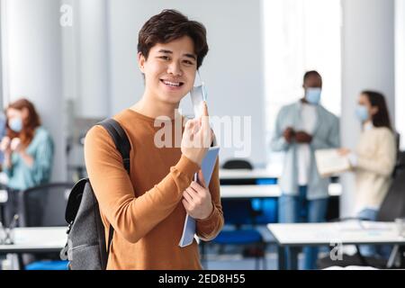 Un homme asiatique souriant prend un masque médical jetable en classe Banque D'Images