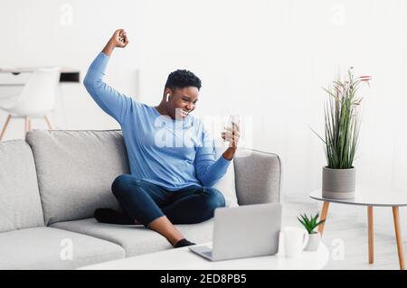 Femme noire excitée portant un casque à l'aide d'un téléphone Banque D'Images