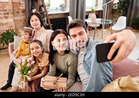 Bonne famille de cinq personnes assises en rangée sur grand doux canapé confortable dans le salon et vue sur la caméra de smartphone tout en faisant le selfie à la maison Banque D'Images