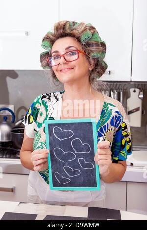 femme au foyer mature avec des curlers montre une planche avec des coeurs Banque D'Images