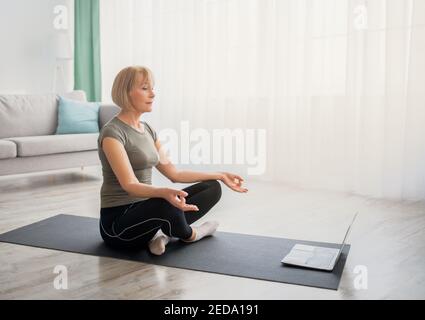 Paisible femme âgée méditant avec les yeux fermés devant l'ordinateur portable à la maison, espace de copie Banque D'Images