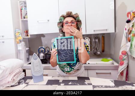 femme au foyer mature avec des curlers montre une planche avec des coeurs Banque D'Images