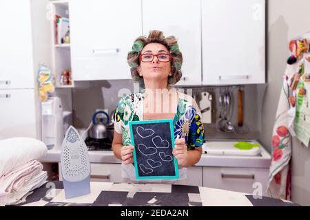 femme au foyer mature avec des curlers montre une planche avec des coeurs Banque D'Images