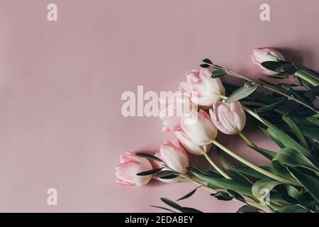 Photo de stock au style naturel. Pâques féminine, composition printanière avec bouquet de tulipes et branches d'olivier sur fond de table rose. Cadre fleuri Banque D'Images