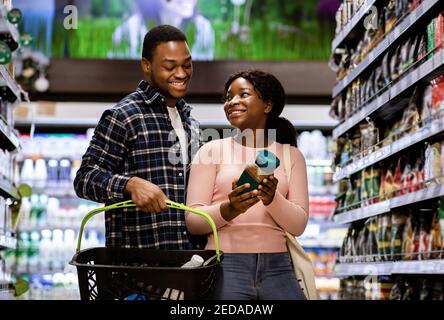 Un couple noir positif avec un panier de courses au supermarché Banque D'Images