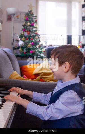 Garçon jouant du piano dans un salon avec un Arbre de Noël en arrière-plan Banque D'Images