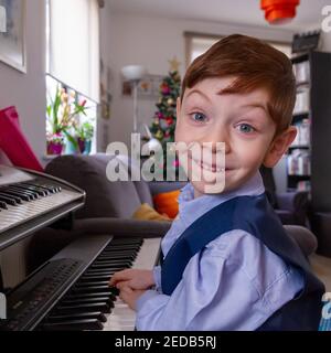 Garçon jouant du piano dans un salon avec un Arbre de Noël en arrière-plan Banque D'Images