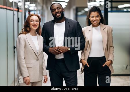 Des collègues qui réussissent en toute confiance se trouvent dans un bureau moderne. Portrait de gens d'affaires souriants multiethniques en tenue formelle. Les employés amicaux, hommes et femmes, regardent le concept de caméra et de travail d'équipe Banque D'Images