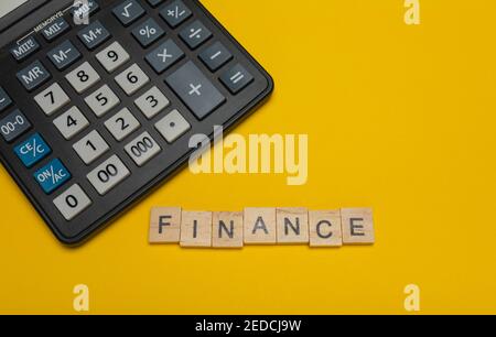 Expression ou mot - finance. Bloc de lettres en bois et calculatrice moderne sur fond jaune, concept d'affaires avec espace pour le texte Banque D'Images