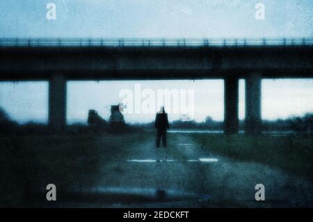 Une figure de moody, de retour à la caméra. Debout sous un pont dans un paysage post-industriel. Avec un grunge, résumé, modifier. Banque D'Images