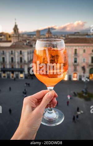 Femme tenant un verre d'Aperol Spritz avec vue sur le paysage urbain de Catane en Sicile, Italie Banque D'Images