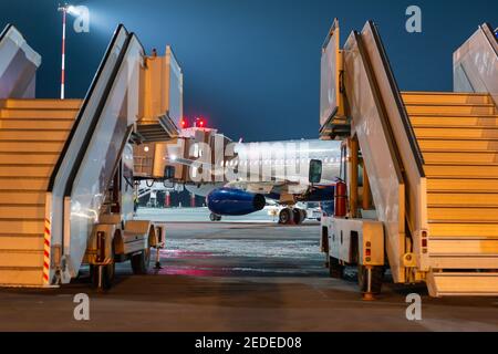 Une vue derrière les rampes de passagers mobiles à l'avion avion se tenant à la passerelle d'embarquement sur l'aéroport de nuit tablier Banque D'Images