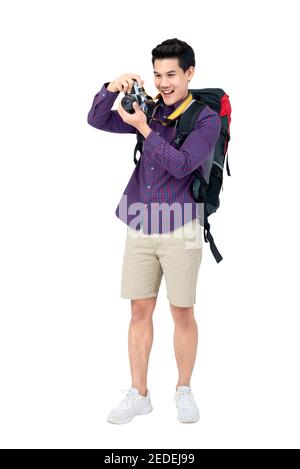 Portrait isolé de jeune heureux attrayant homme touristique asiatique dedans tenue décontractée portant un sac à dos prenant une photo avec son appareil photo Banque D'Images