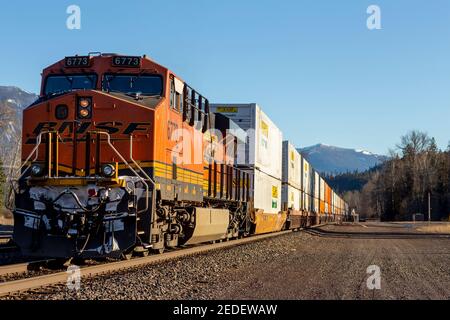 Une locomotive de poussée tractée, 6773 ans, d'un train de fret à conteneurs intermodal BNSF descendant les voies dans la ville de Troy, Montana. Banque D'Images